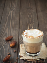 Glass cup of coffee with milk on a dark wooden background. Hot latte or cappuccino prepared with milk on a rustic wooden table with copy space. Near dates fruits.