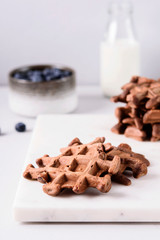 Homemade Chocolate waffles, milk and blueberries on white marble tray. Breakfast. Selective focus