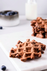 Homemade Chocolate waffles, milk and blueberries on white marble tray. Breakfast. Selective focus