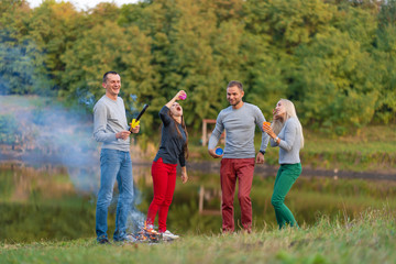 Obraz premium Picnic with friends in at lake near bonfire. Company friends having hike picnic nature background. Hikers relaxing during drink time. Summer picnic. Fun time with friends