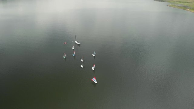 Aerial footage of a fleet of small sailboats in the middle of a lake