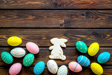 Easter symbols. Painted eggs and bunny gingerbread on dark wooden desk top-down frame copy space