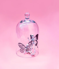 fairy skeletons under glass dome on pink background. surreal creative image. close up