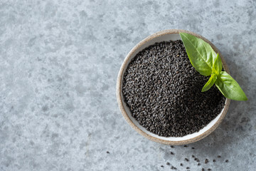 Basil edible seeds in bowl with fresh leaves. View from above.