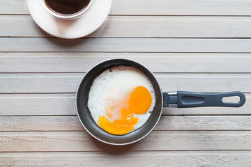 cup of coffee and fried egg in frying pan on wooden table