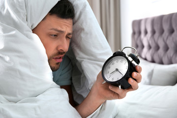 Sleepy man with alarm clock at home in morning