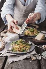 Woman cooking soy noodles, fried garlic, Brussels sprouts and chesse in a serving plate on a cutting board, forks and spoons vegan concept in a rustic style