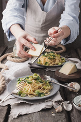 Chef hands cooking Italian pasta and adding cheese parmesan in dish on wooden table background. Chef serving homemade italian with brussels sprouts and cheese pasta on plate