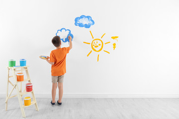 Little child painting cloud on white wall in room