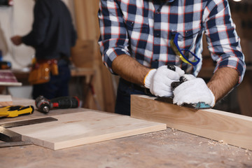 Professional carpenter grinding wooden plank with jack plane in workshop, closeup