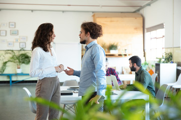 Side view of serious man talking with confident colleague. Two coworkers communicating in open space office. Communication concept