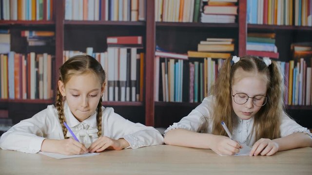 Small girl peeping at her classmate during exam. Little schoolchildren passing test. Cheating on exam concept. Schoolgirls wryting cheat sheet quiz paper for exam test