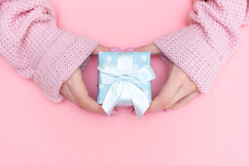 White gift box with red bow in the children's hands on pink background