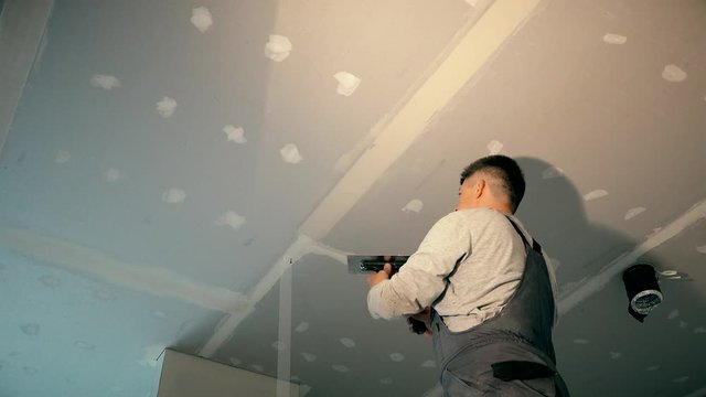 Professional worker smoothing gypsum plasterboard frame with spackling paste
