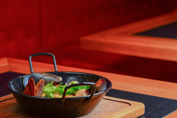 Couscous with seafood in a bowl. Three clams served in a restaurant on wooden cutting board on rustic dark table.