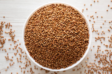 Uncooked Roasted Buckwheat in a white bowl on a white wooden background, top view. Flat lay, overhead, from above. Close-up.