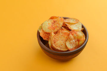 Potato chips, crisp unhealthy chips, junk food, fast food concept. Potato chips in a bowl over bright yellow background.
