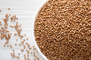 Uncooked Roasted Buckwheat in a white bowl on a white wooden background, top view. Flat lay, overhead, from above. Close-up.