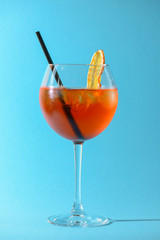 A glass of fruit liqueur in wine glass with a piece of lemon and black plastic straw isolated on pastel blue background.