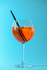 A glass of fruit liqueur in wine glass with a piece of lemon and black plastic straw isolated on pastel blue background.