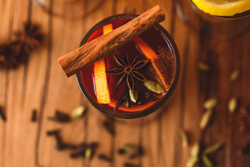 One glass of hot red mulled wine with fruit and spices on wooden table on colorful orange...