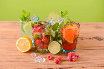 Four tropical mixed drinks, orange, lemon and raspberries cocktails over bright pastel green background.