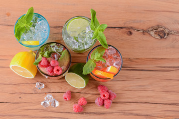 Four tropical mixed drinks, orange, lemon and raspberries cocktails over bright pastel green background.