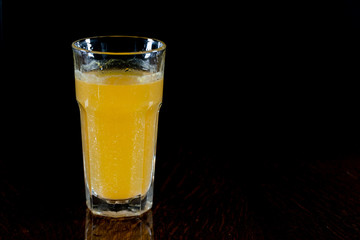 Orange drink in a glass. Glass on a black background. The tablet dissolved in water. Non-alcoholic healthy tonic drink.