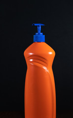 Orange bottle of detergent. Bottle without labels and name. Hand squeezes the detergent. Dishwashing liquid. House cleaning.