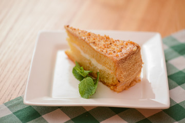 Slice of victoria sponge cake with cream filling, served with a mint leaf on a white plate on light wooden table