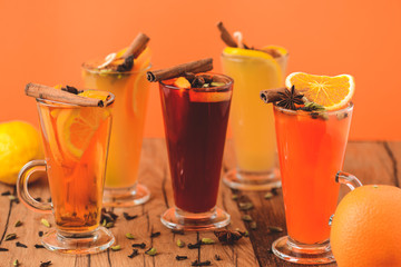 Five glasses of hot red mulled wine with fruit and spices, mango martini on table on orange background. Copy space.