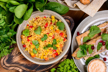 Georgian vegetarian bulgur with vegetables - tomatoes carrots zucchini yellow bell pepper and fresh basil on a table