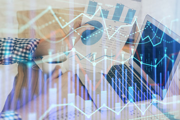 Double exposure of stock graph with businessman typing on computer in office on background. Concept of hard work.