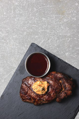 Grilled beef steak medium rare with sauce on black wooden cutting board. Top view, copy space, flat lay.