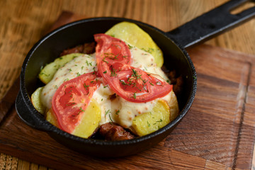 Meat and mushroom gratin with cheese and tomatoes served in a pan over dark wooden table background. Ukrainian cuisine.