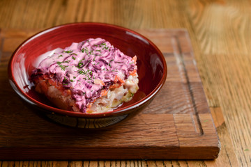 Traditional Russian herring salad served in a bowl on dark wooden table background in a restaurant.