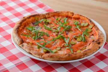 Delicious Italian pizza with salmon fish served on white plate on rustic wooden table with plaid tablecloth.