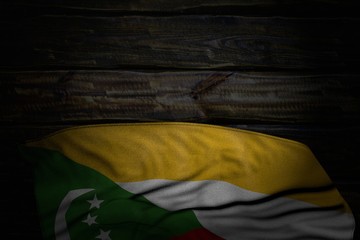 nice dark photo of Comoros flag with big folds on old wood with empty place for content - any celebration flag 3d illustration..
