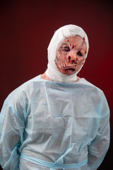 Crazy zombie horror make up. Person in blue madical shirt and bandaged head. Scars, deep scratches...