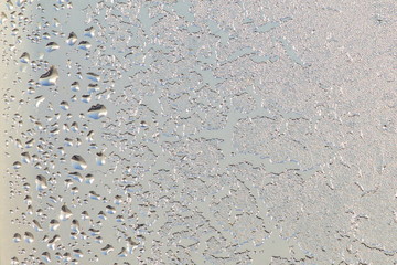 Blue window glass covered hoarfrost ice pattern texture with water drops. Cold nature winter background