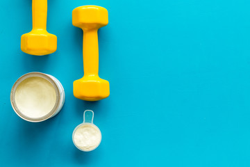 Sport nutrition. Whey protein, shaker, dumbbells on blue background top-down flay lay copy space