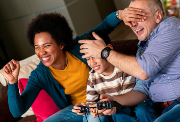 Smiling mixed race family enjoying time at home sitting on sofa in living room and playing video games.