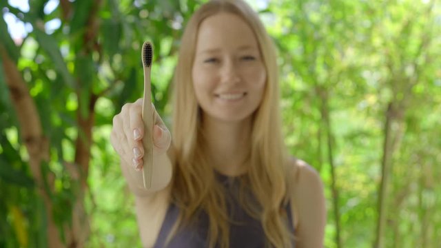 A young woman shows a wooden toothbrush made out of bamboo. Concept of eco friendly zero waste bamboo products