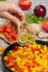 Hand pours oil. Sliced tomatoes and greens in pan