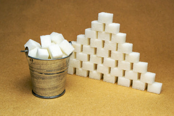  Bucket with sugar cubes and sugar cubes laid out by a pyramid on a beige background