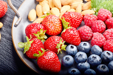 Tray with ripe organic bilberry raspberry strawberry and almonds set on slate closeup