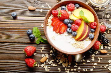 Flat lay of fruit healthy muesli with peaches strawberry almonds and blackberry in clay dish with yogurt