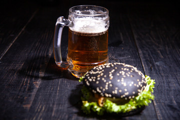 Black burger and glass of beer isolated on black
