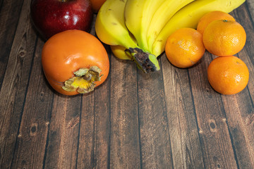 Fruits, bananas, clementines, persimmons and a red apple on a wooden table