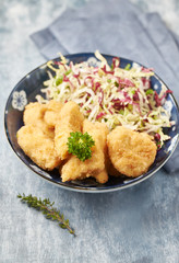 Chicken nuggets with raw salad on bright wooden background
